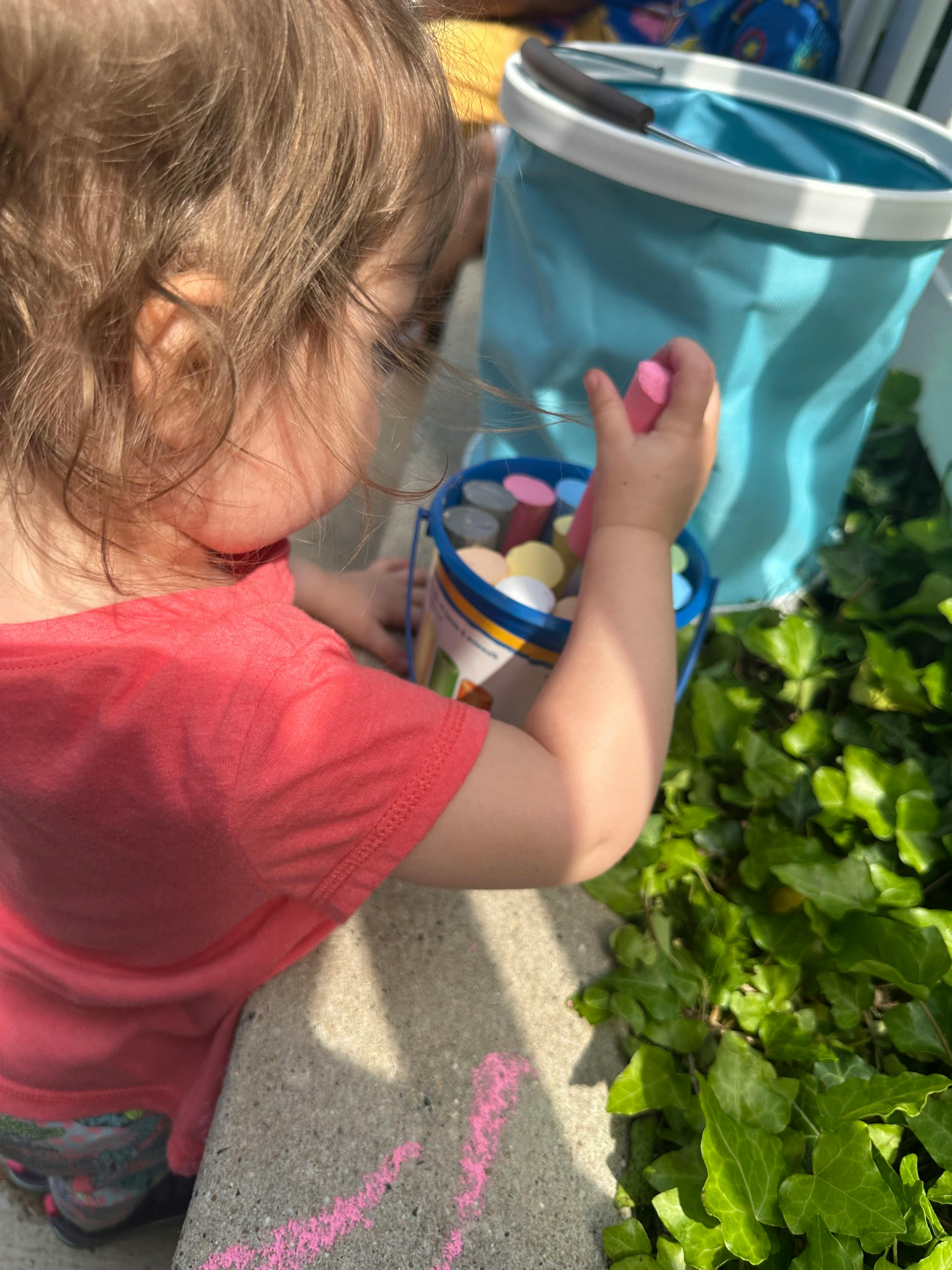 Child holding pink chalk over a bucket of colorful chalk