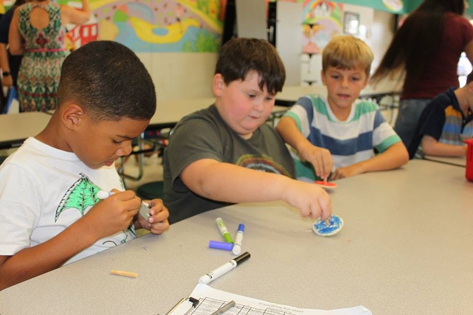 Three children sitting at a table doing an activity
