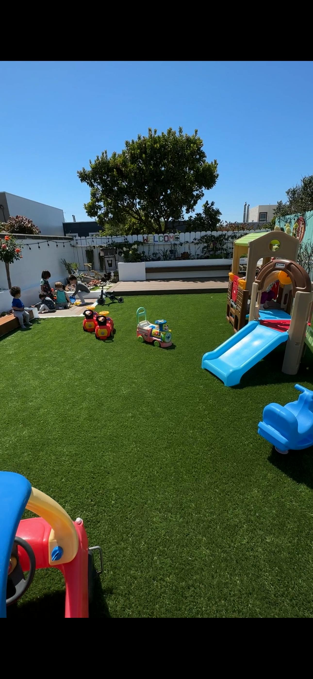 Children playing on a green lawn with a slide and toys