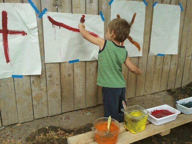Child painting on paper taped to a wooden fence