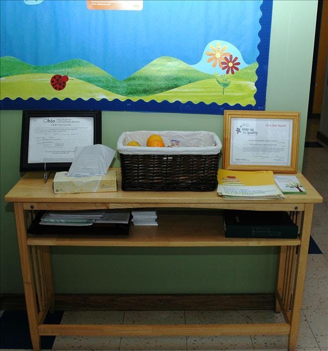 Wooden table with a basket of fruit, tissue box, and framed certificates