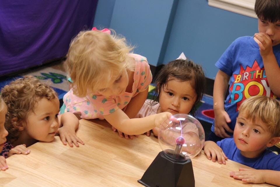 Children gathered around a plasma ball on a table