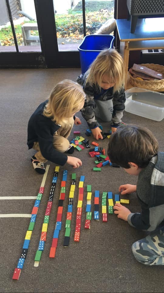 Three children playing with colorful dominoes on the floor