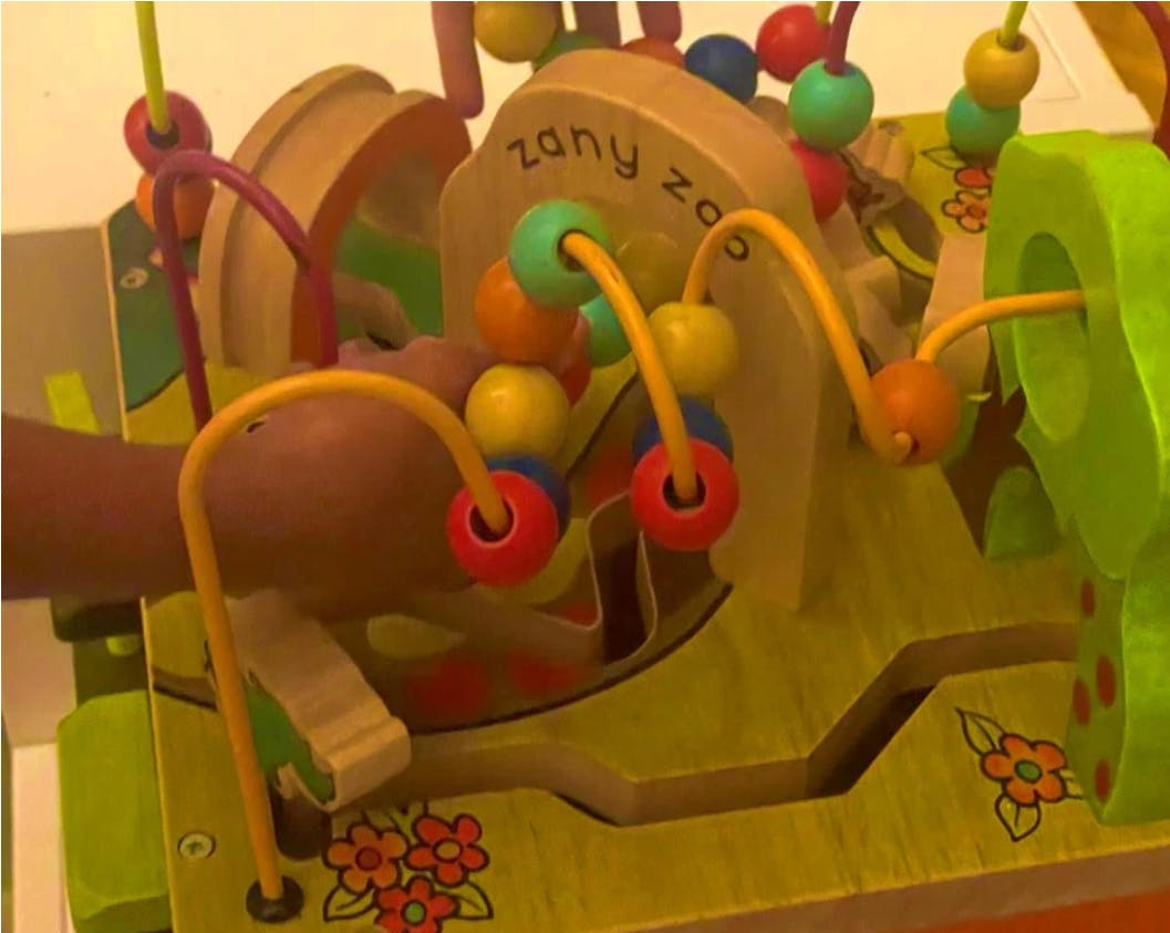 Child's hand playing with a wooden bead maze toy