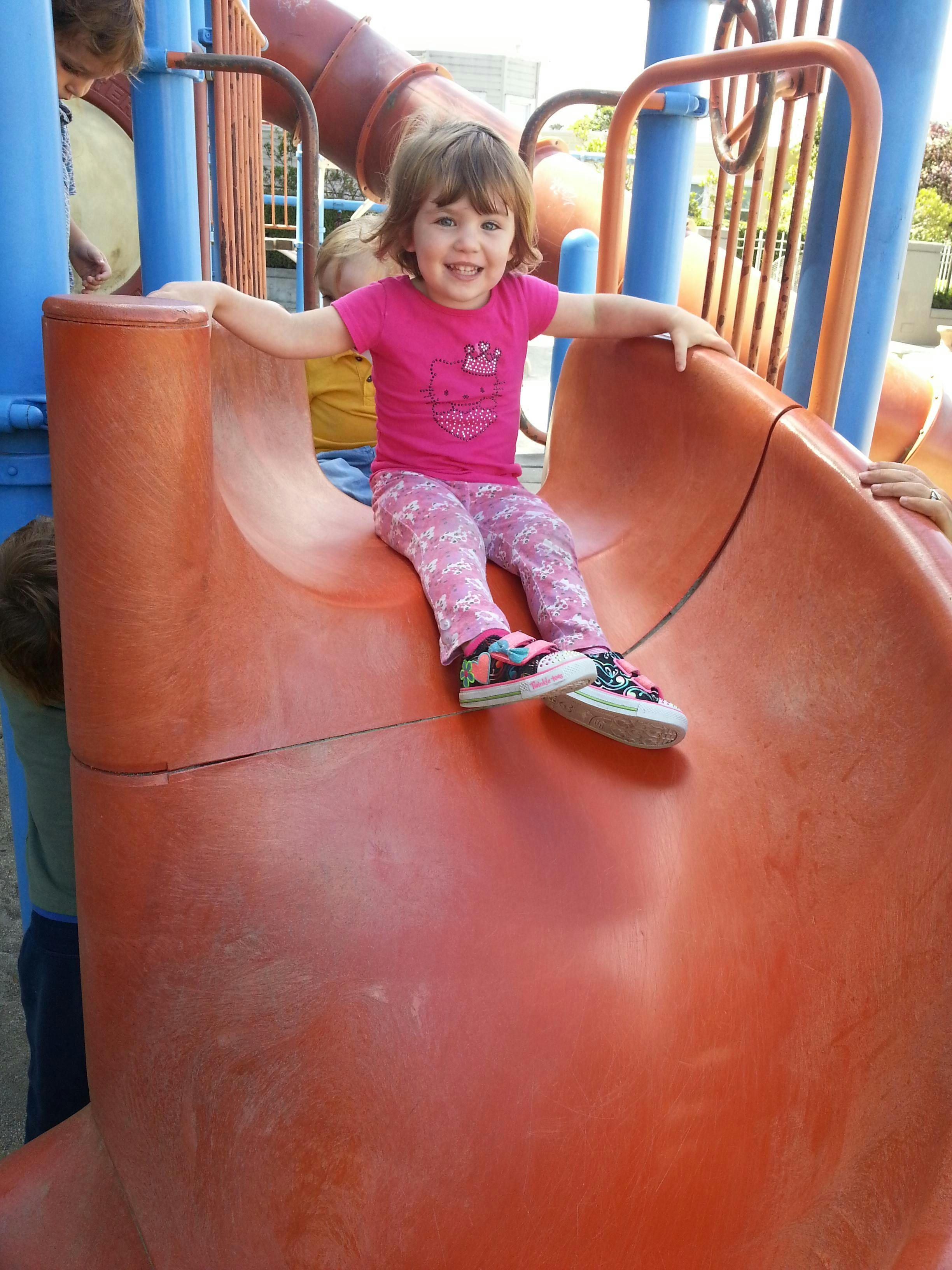 Child sitting at the top of a playground slide