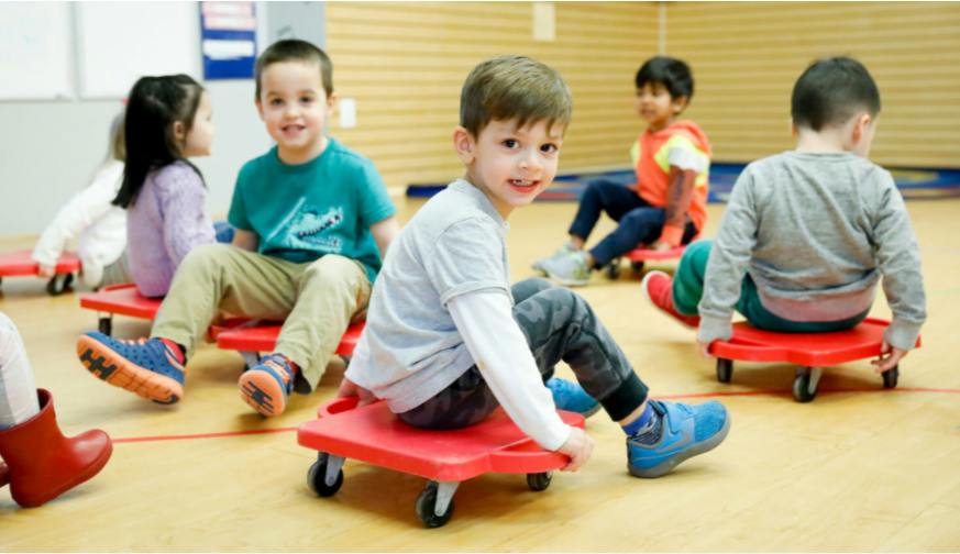 Children sitting on red scooter boards in a classroom