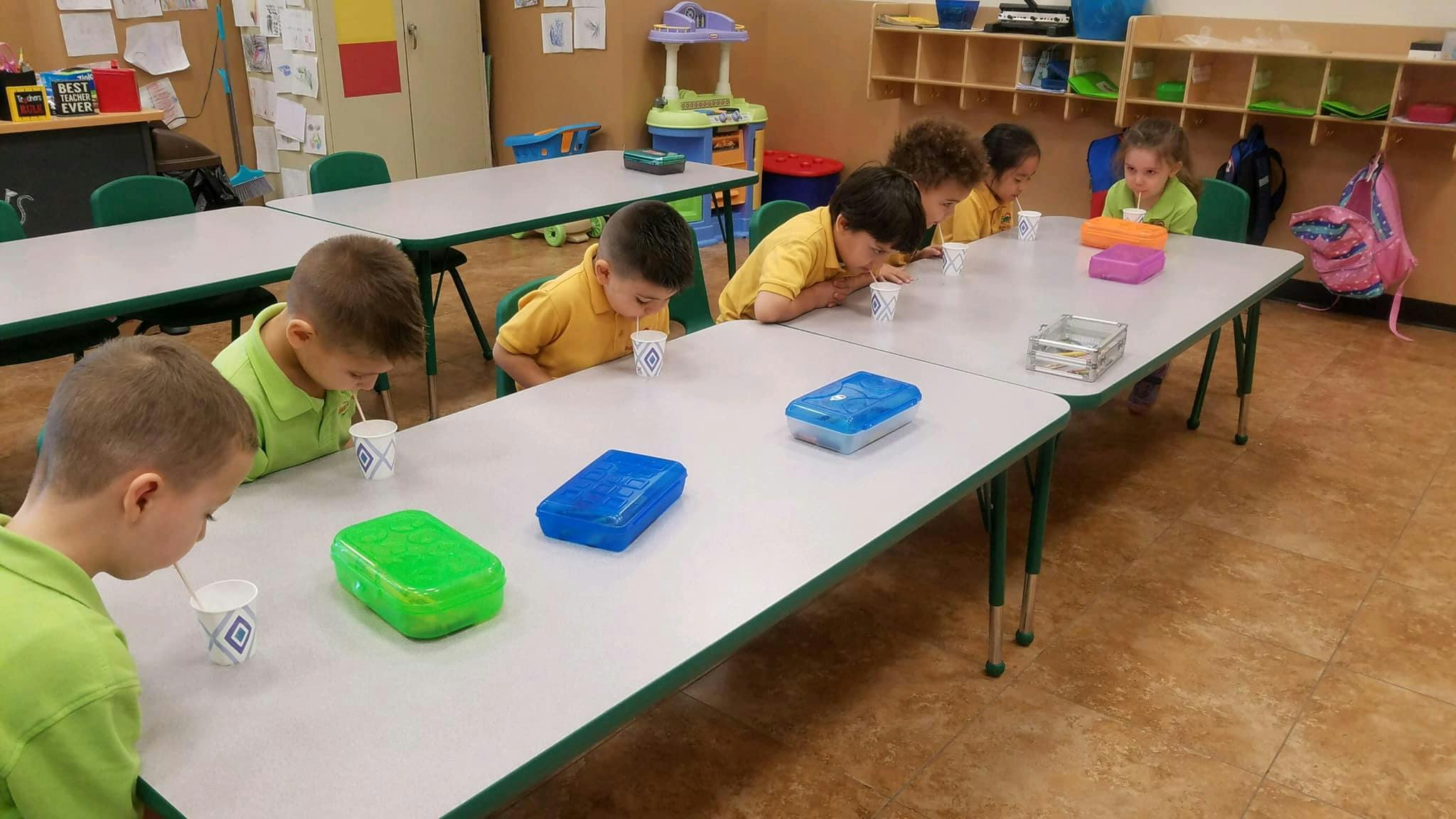 Children drinking from cups at a table in a classroom