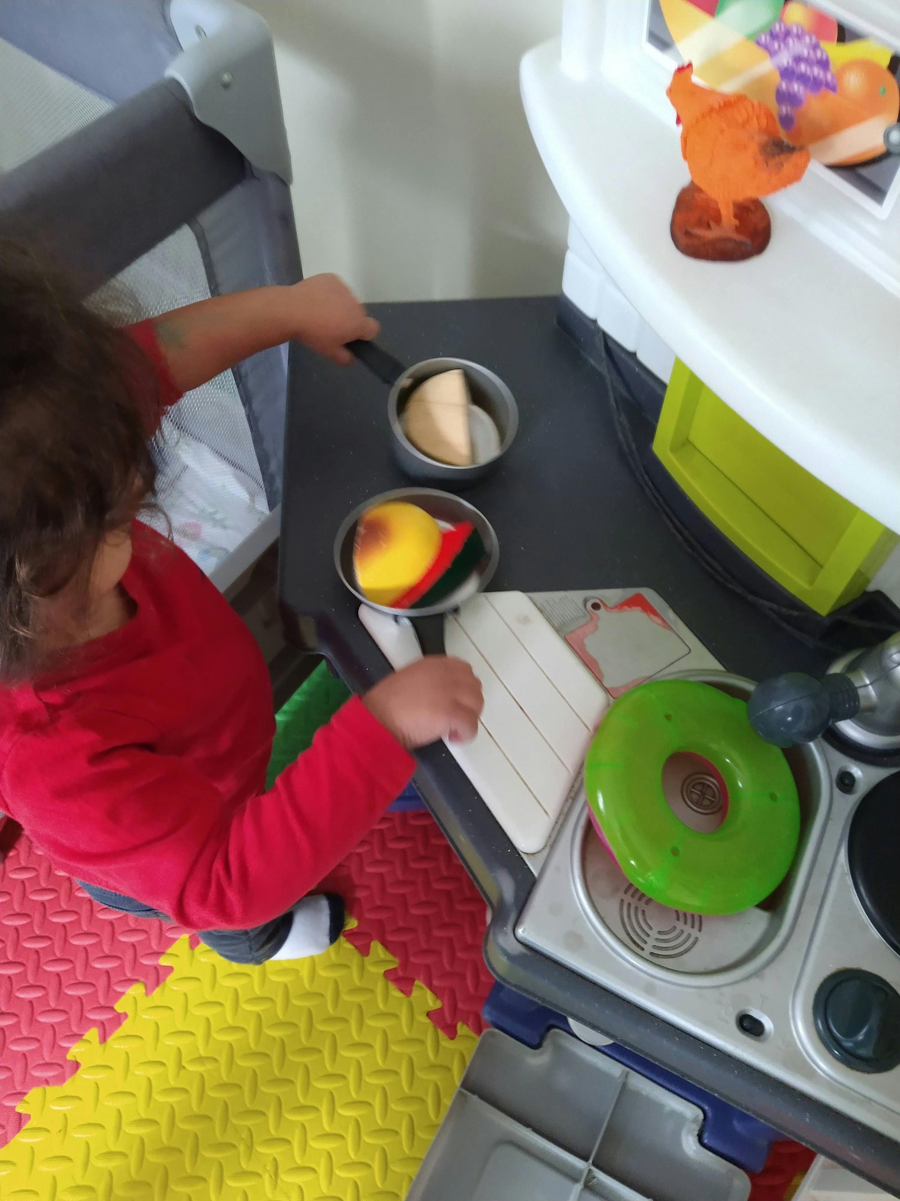 Child playing with a toy kitchen set on a colorful foam mat