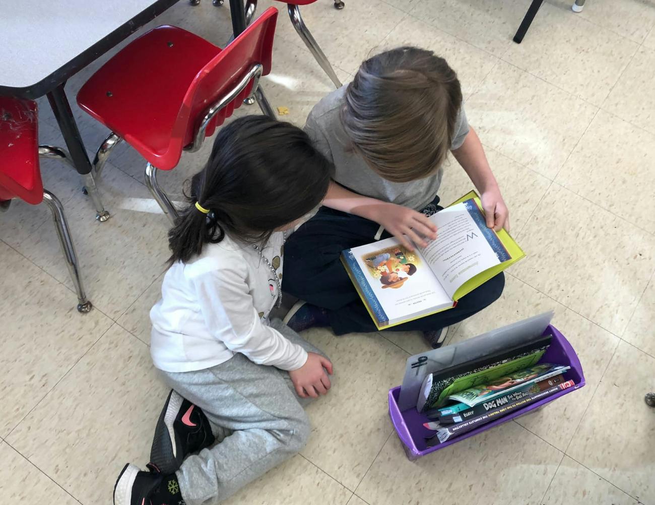 Two children sitting on the floor reading a book together