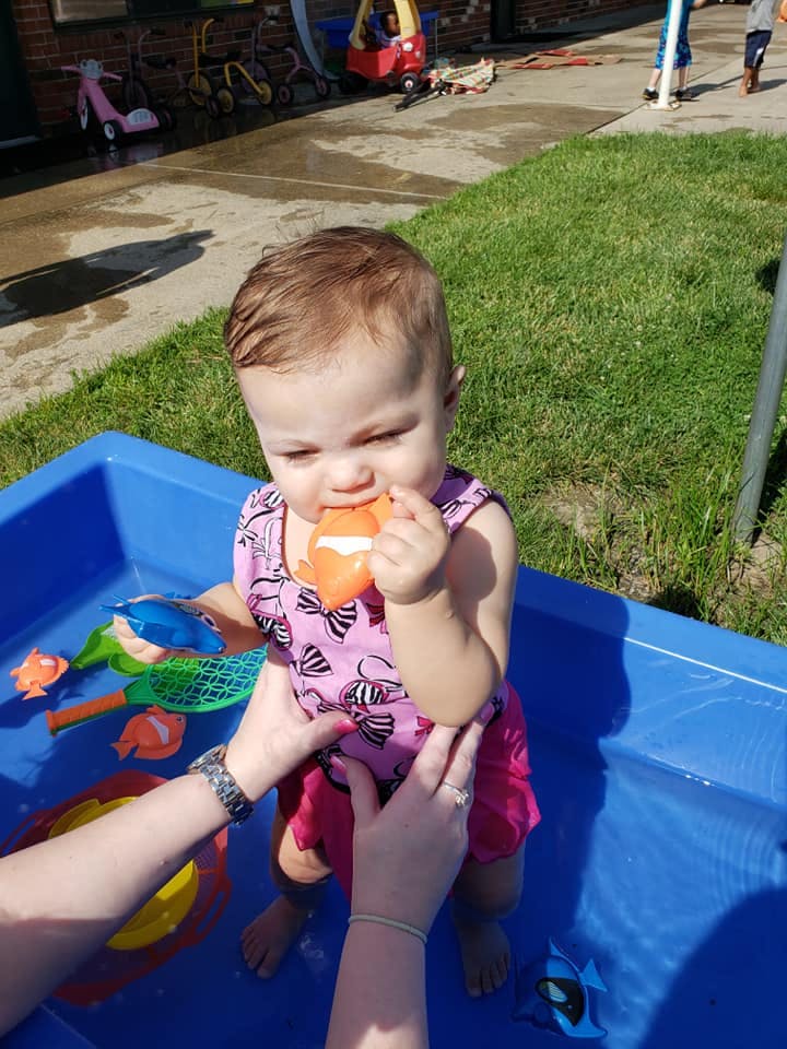 Child in a blue water table holding an orange toy fish