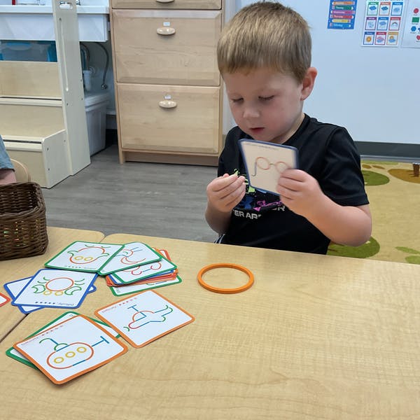 Child holding a card with a drawing of glasses, other cards on a table
