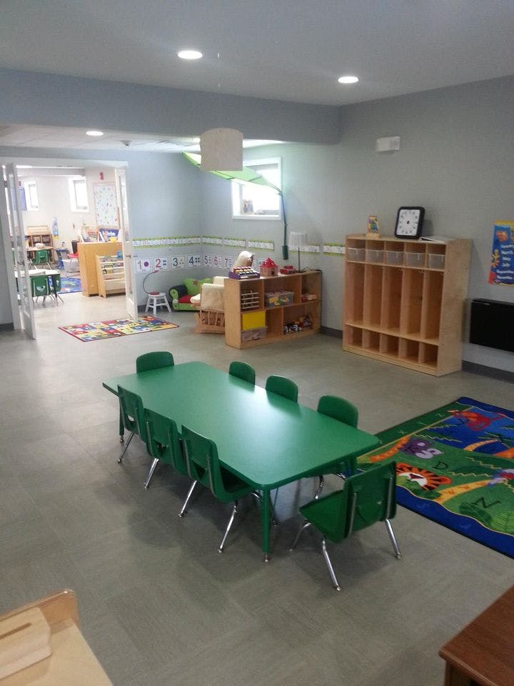 Classroom with green tables and chairs, shelves, and colorful rugs