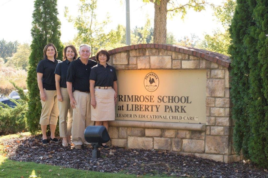 Four people standing next to a stone sign for Primrose School at Liberty Park