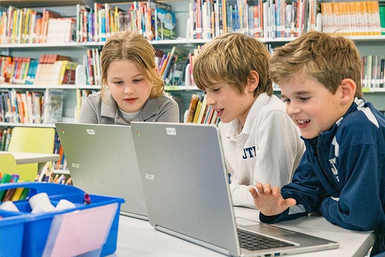 Three children sitting at a table with laptops in a library