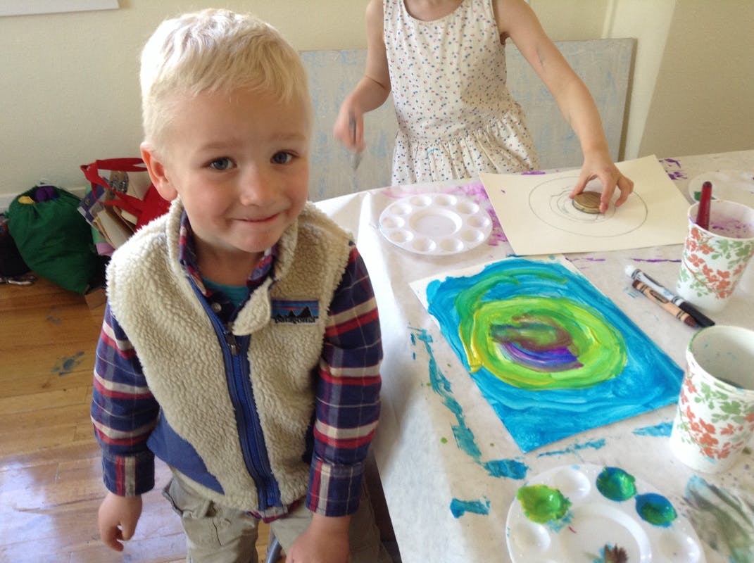 Child standing next to a table with art supplies and a painting