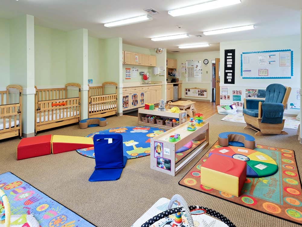 cribs in a daycare room with play mats and toys on the floor
