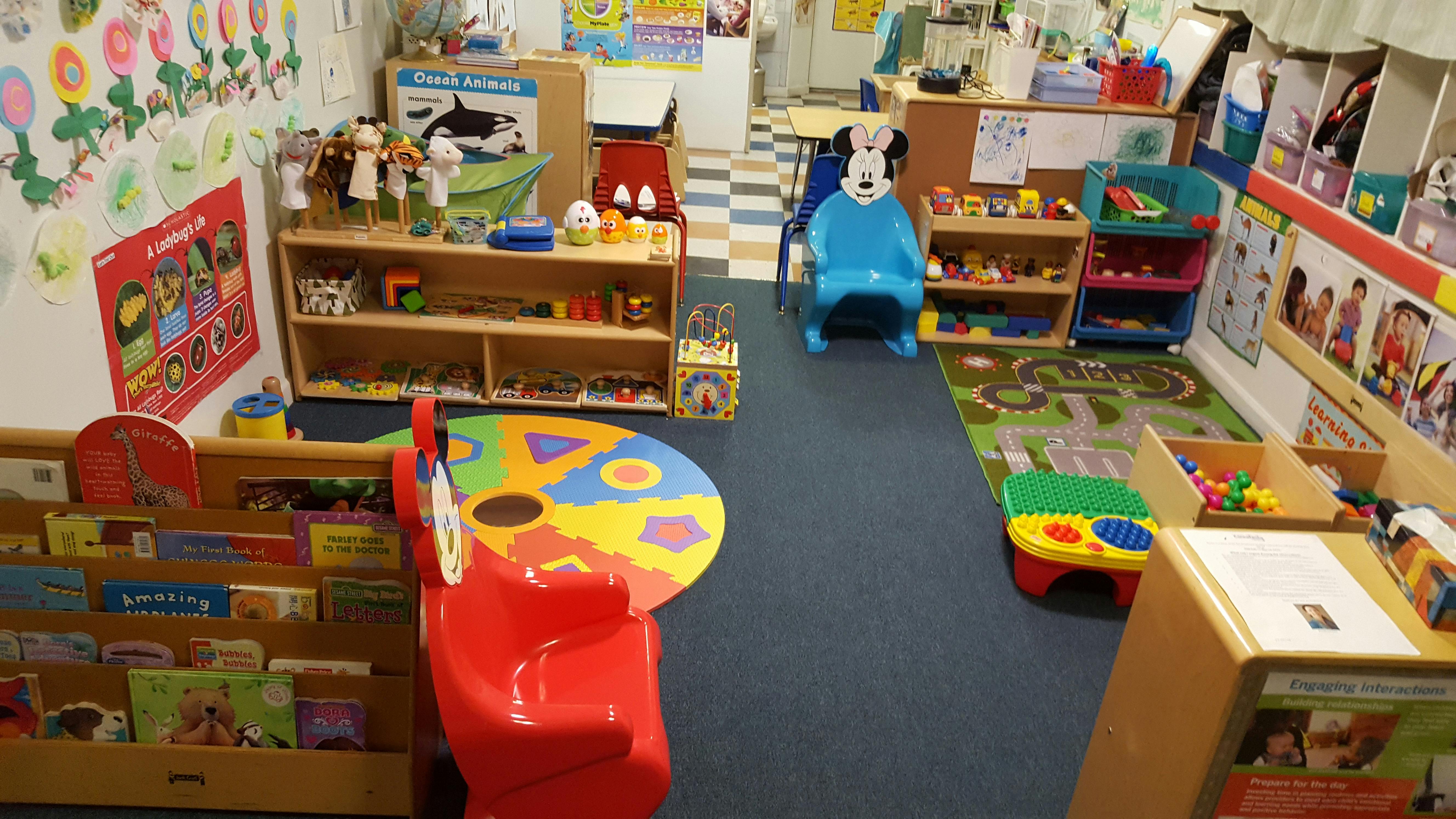 Playroom with shelves of toys and books, colorful rug, and small red chair