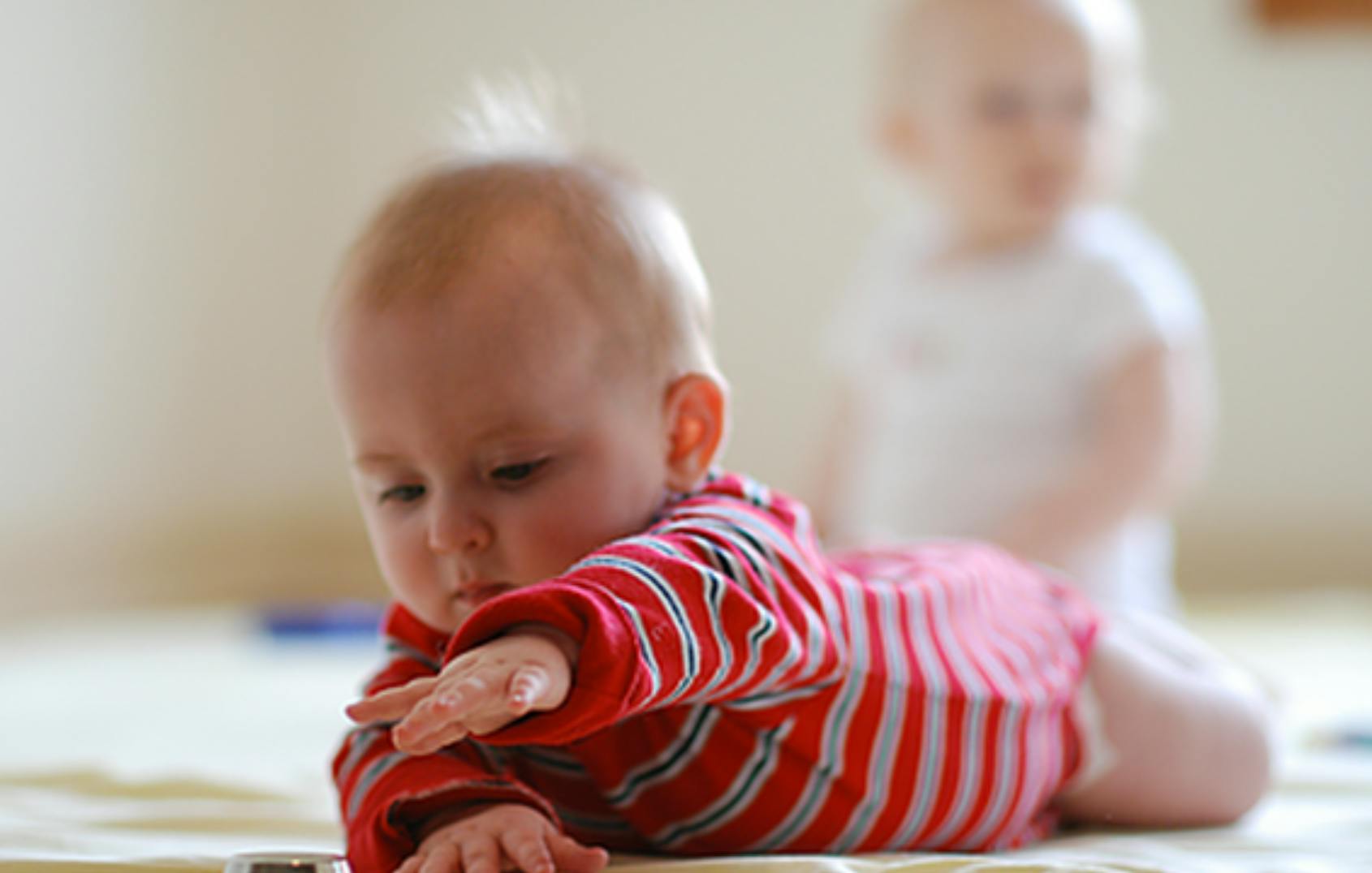Baby in red striped outfit on stomach, another baby in background