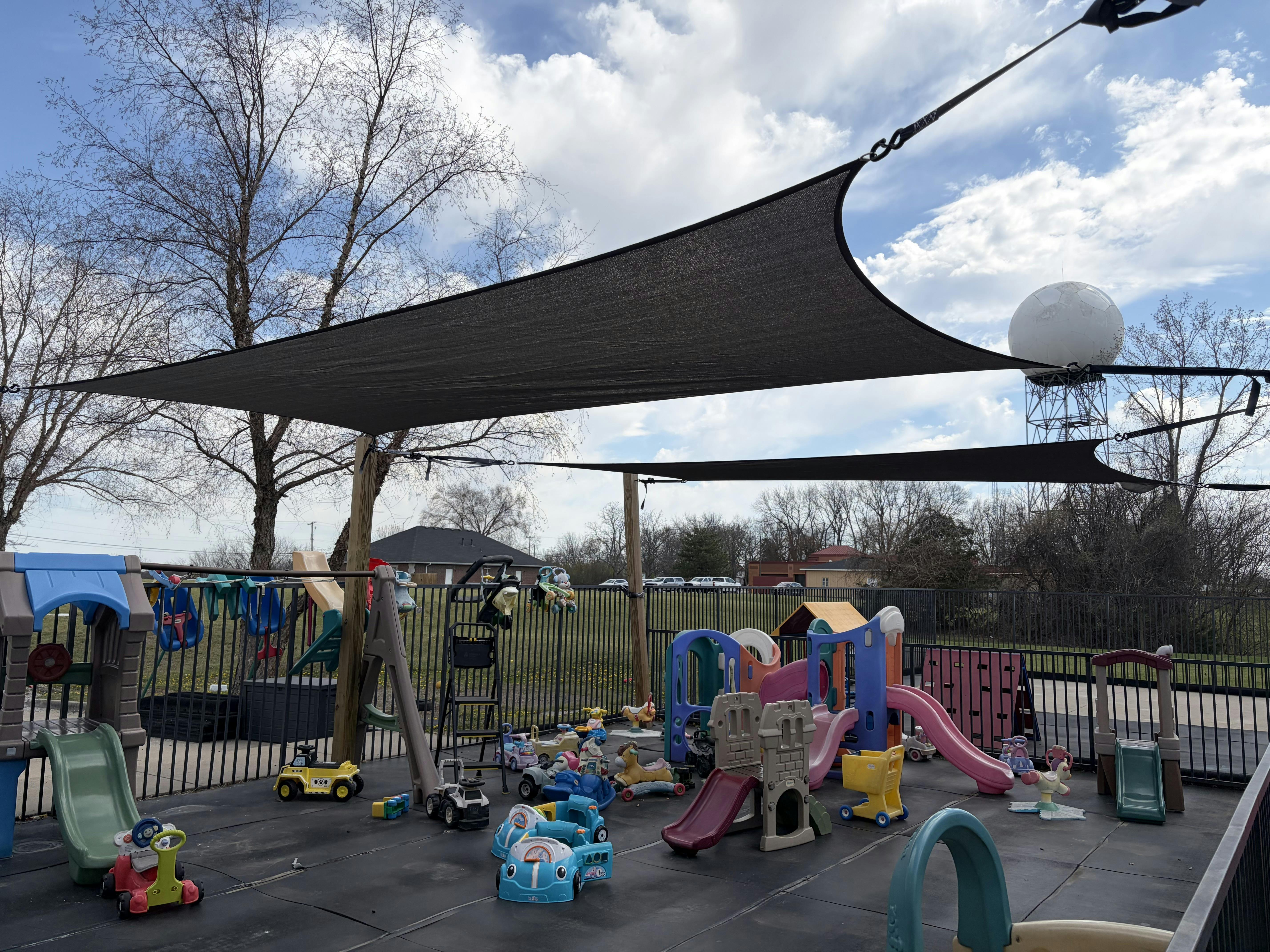 Children's playground with slides, swings, and ride-on toys under a shade sail