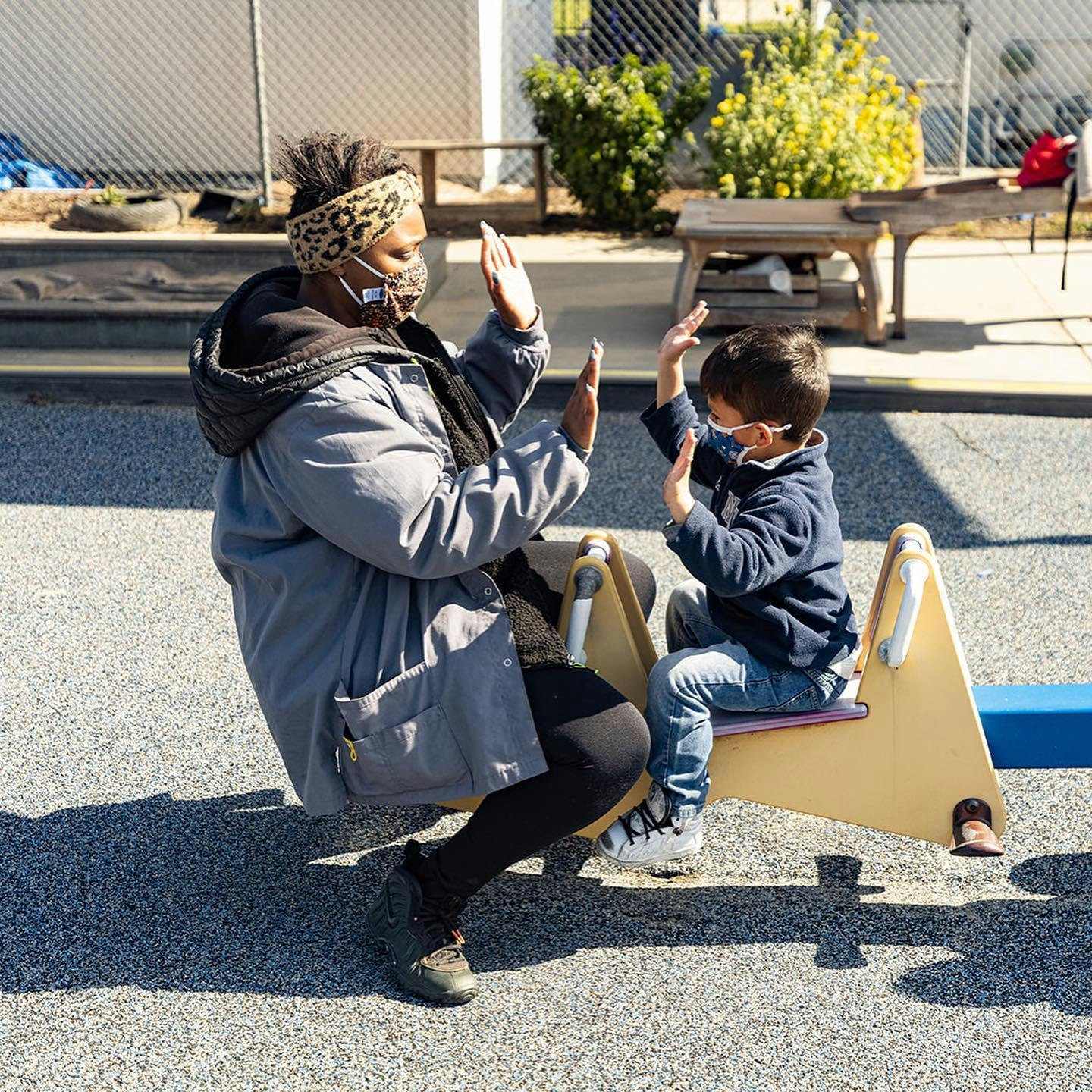 Person and child on a seesaw giving high fives