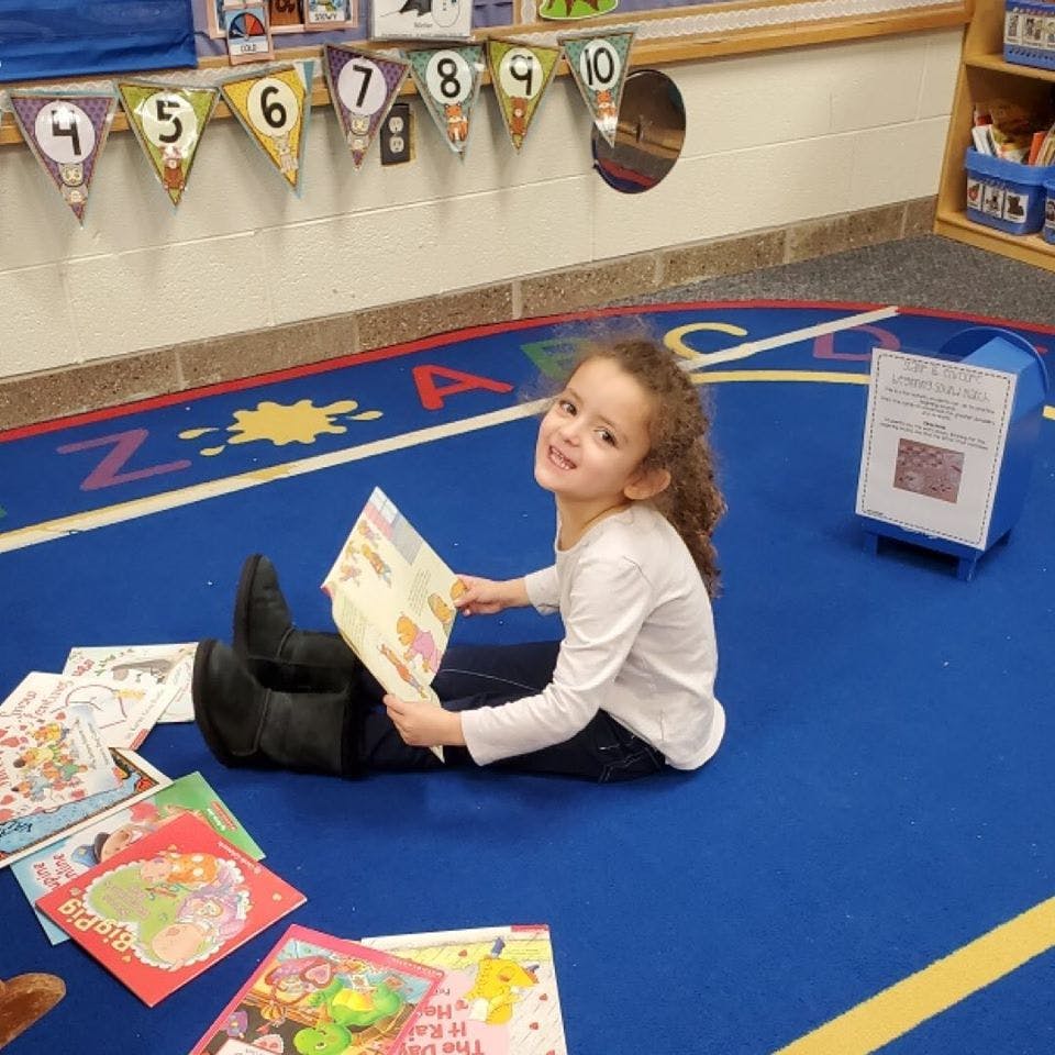 Child sitting on floor reading a book in a classroom