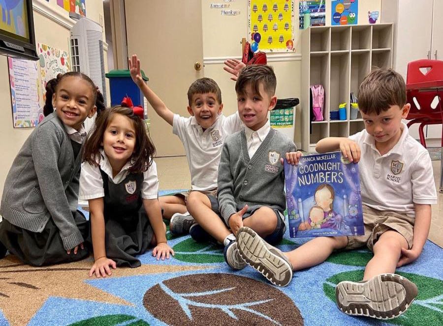 Five children sitting on a rug, one holding a book titled "Goodnight Numbers"