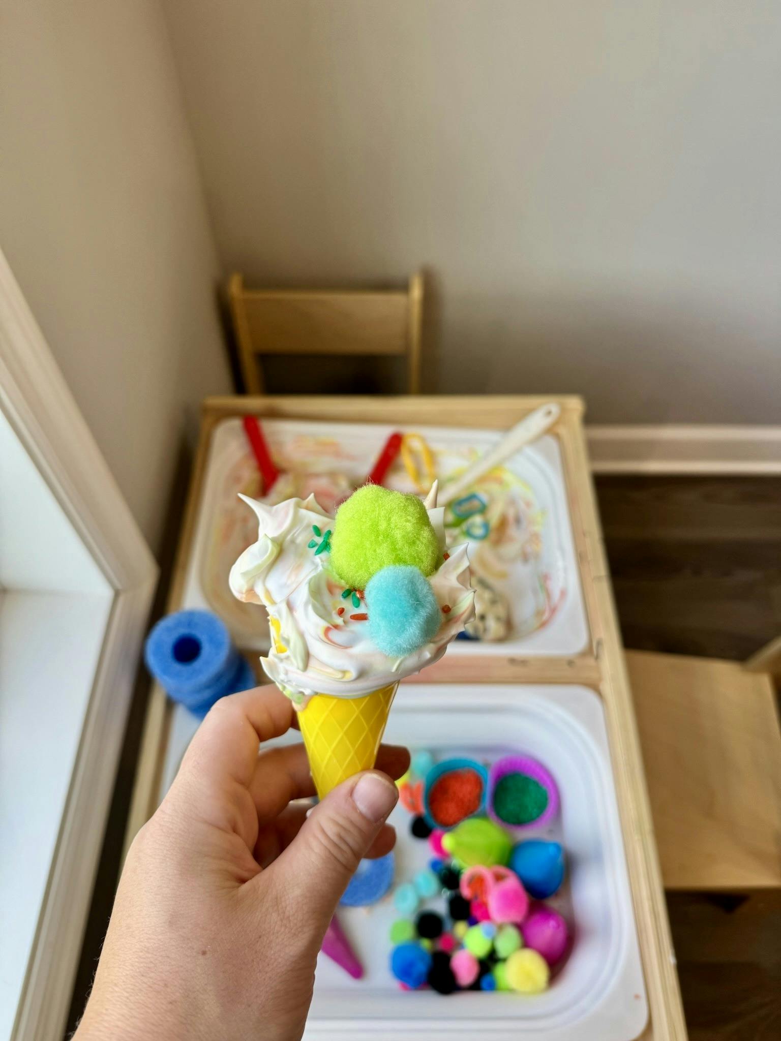 Person holding a toy ice cream cone topped with craft pom-poms