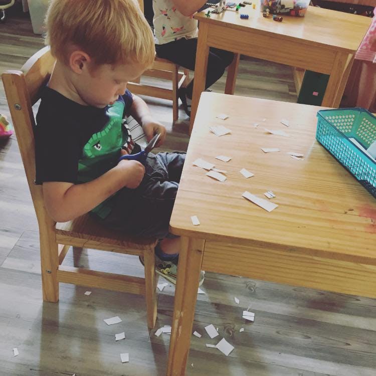 Child sitting at a table cutting paper with scissors