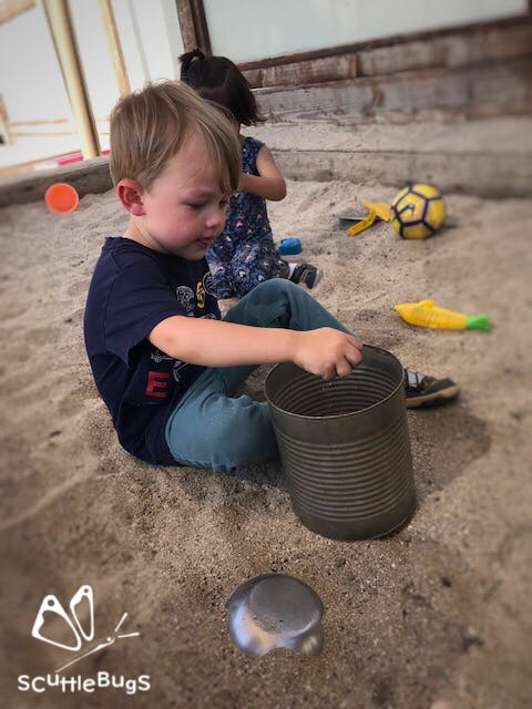 Child sitting in sand holding a large metal can