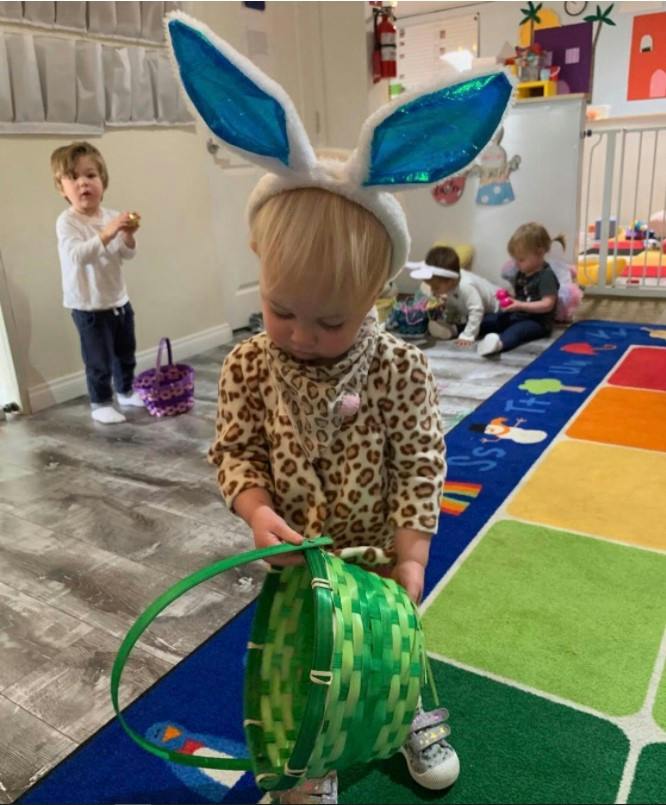 Child wearing bunny ears holding a basket in a play area