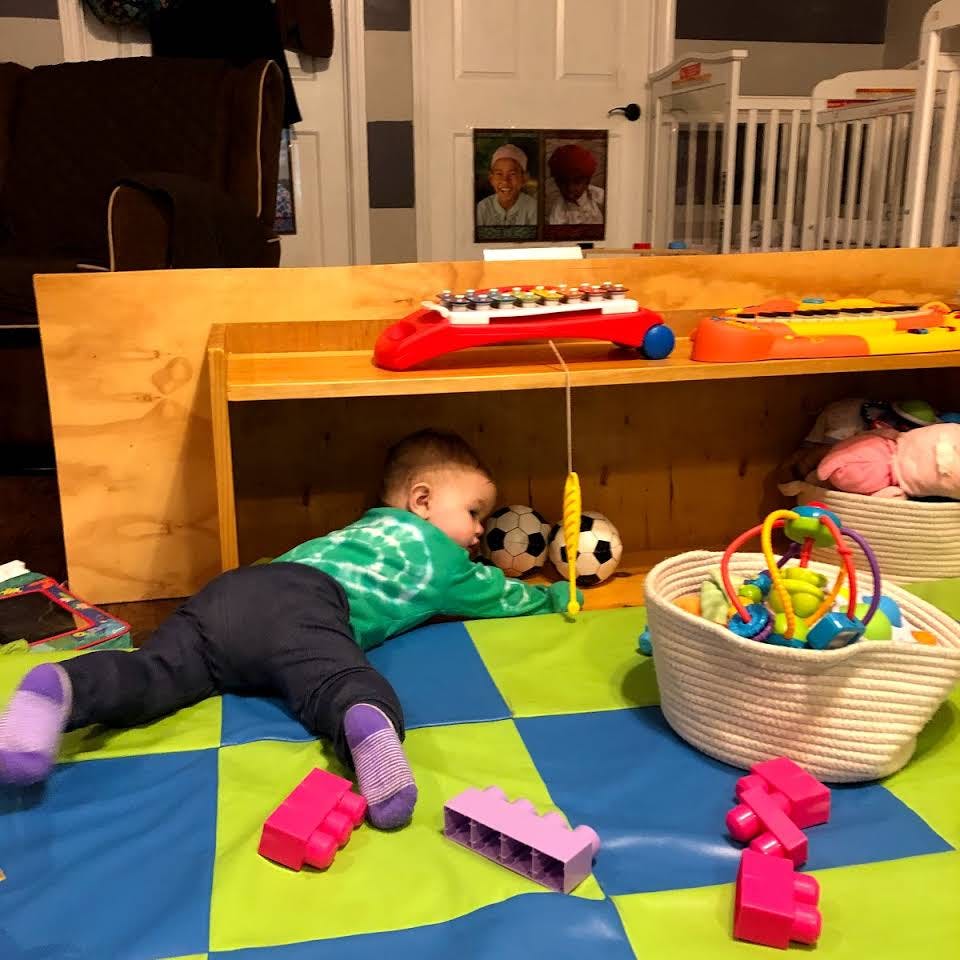 Child lying on floor reaching for toy soccer balls under a shelf