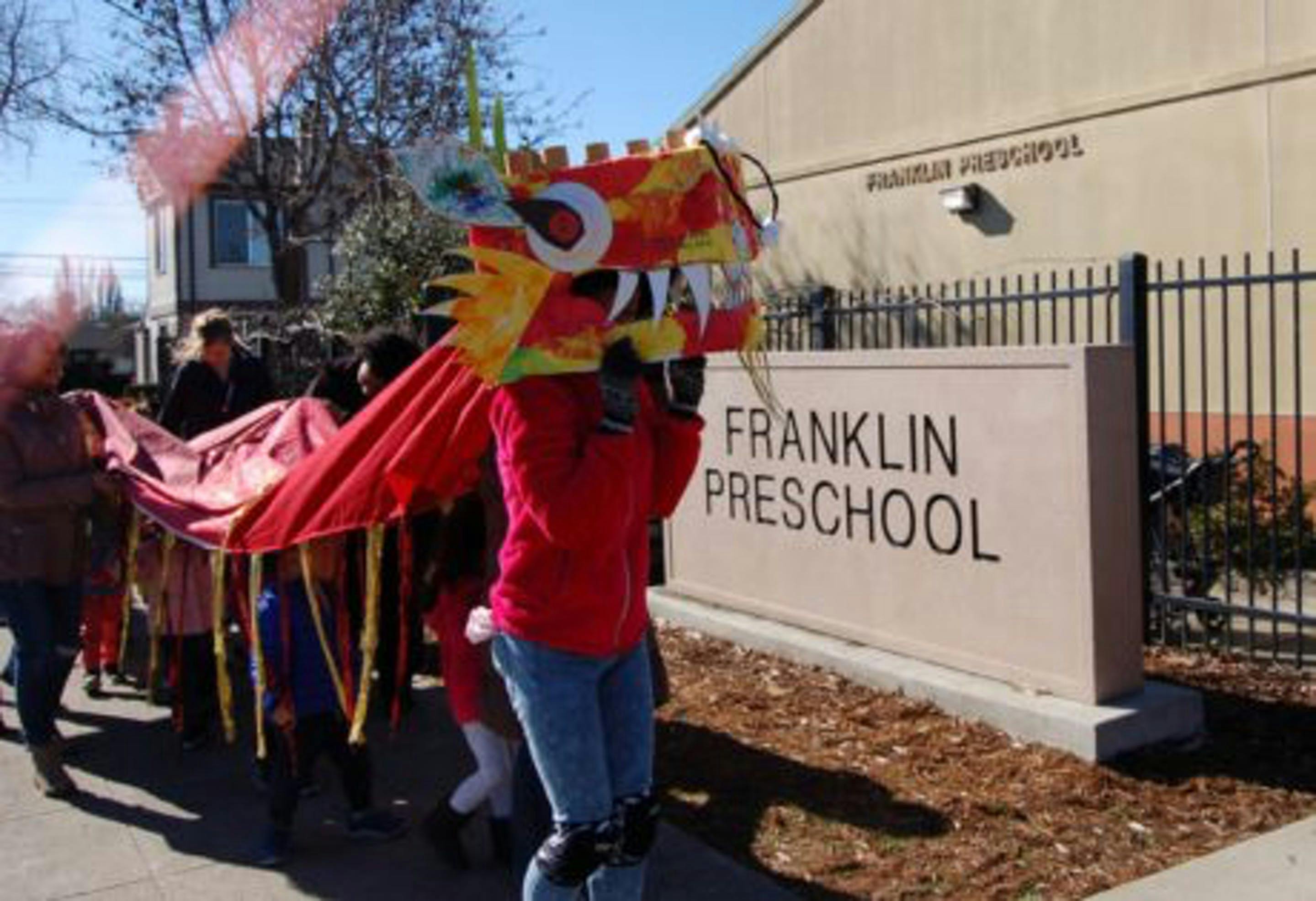 People holding a dragon costume and red fabric in front of Franklin Preschool