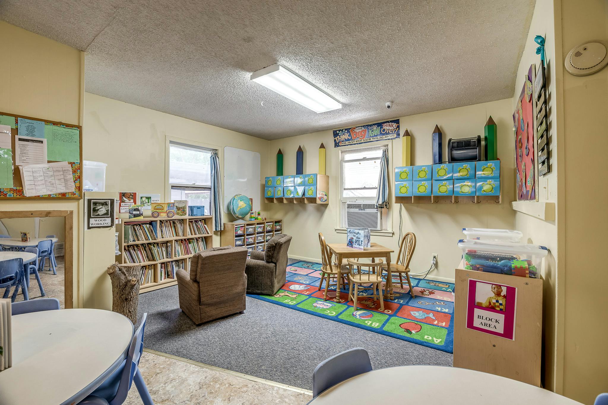 classroom with small tables, chairs, bookshelves, and a colorful rug