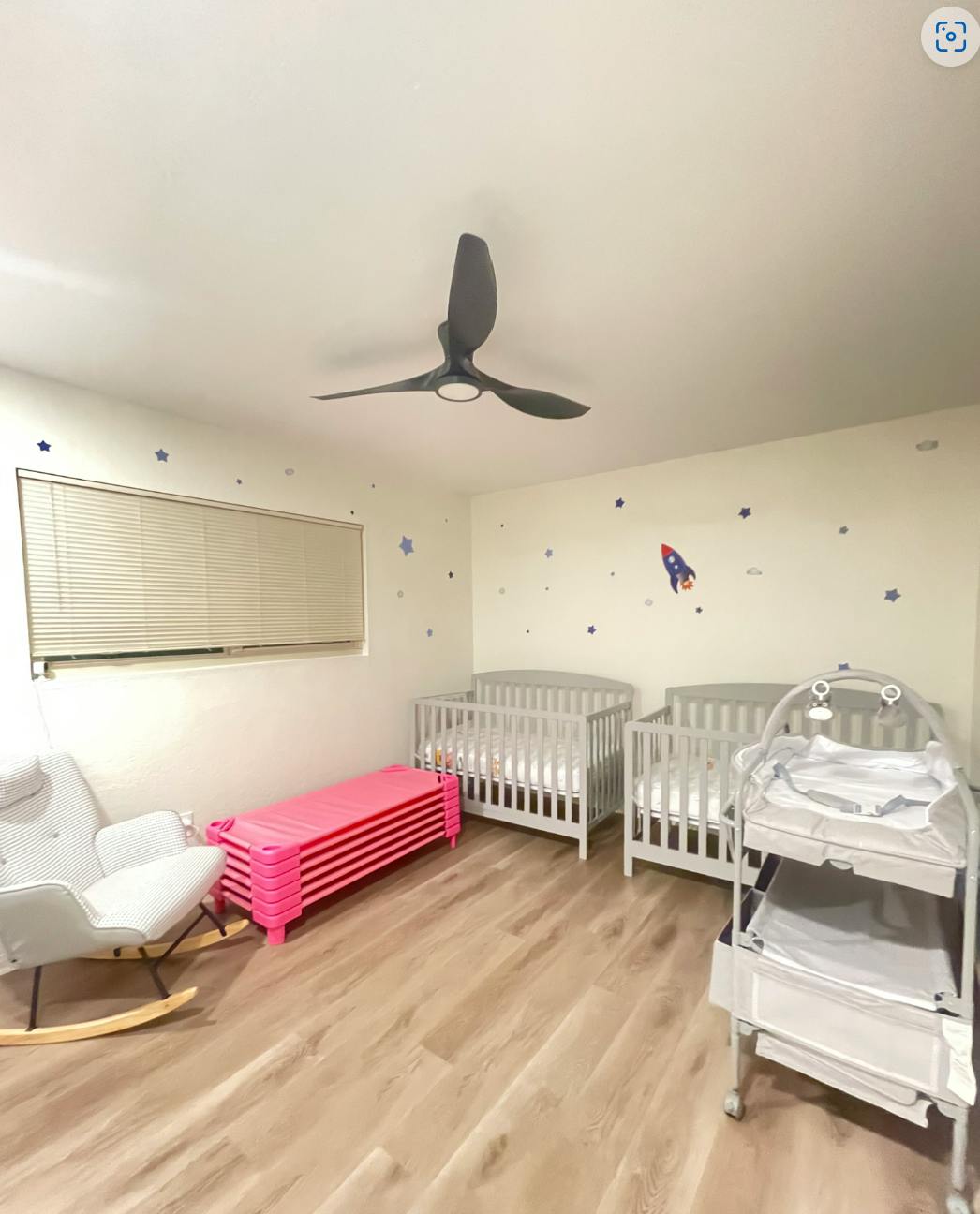 Nursery room with two cribs, a changing table, and a rocking chair