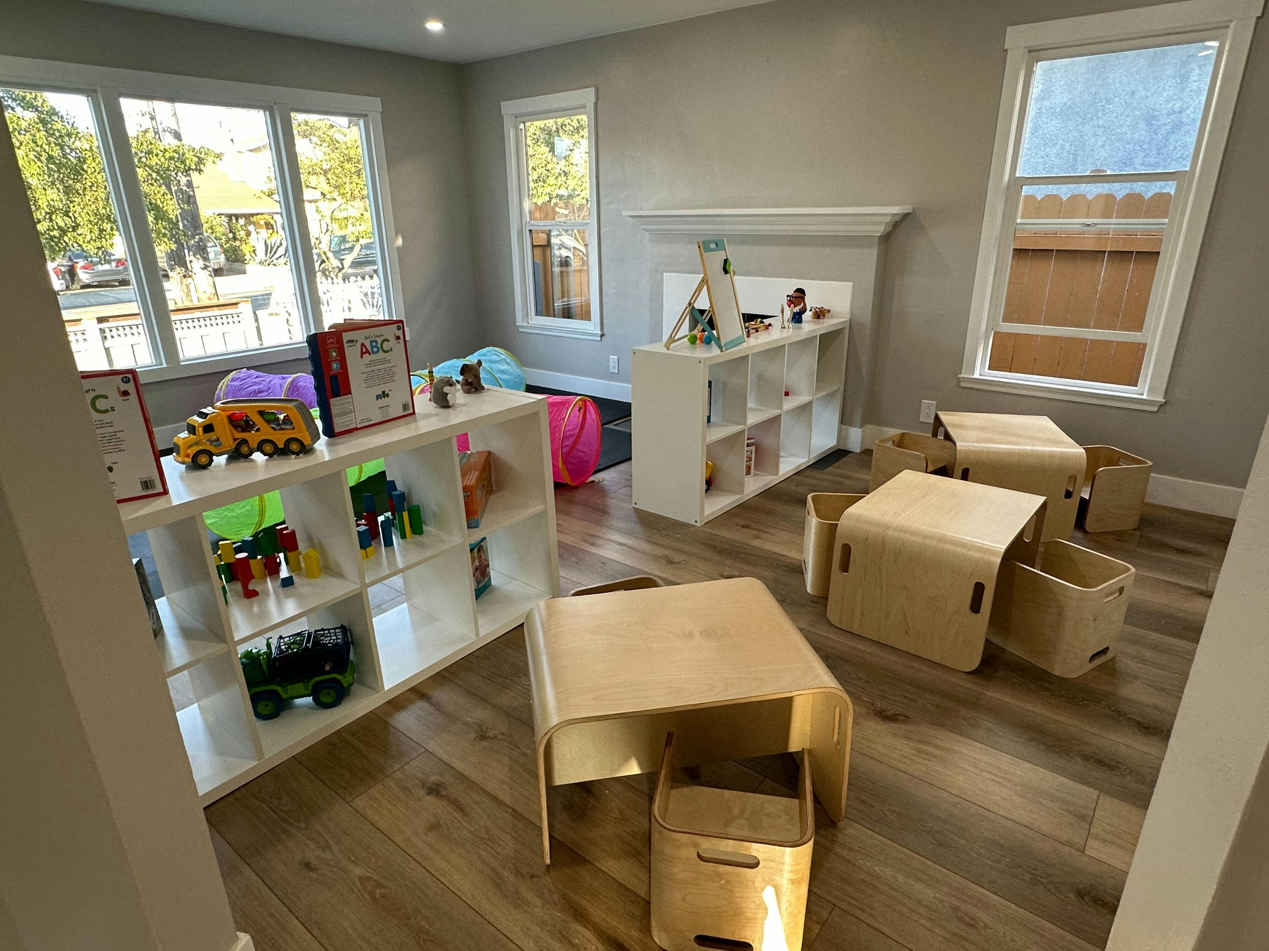 Playroom with wooden tables, chairs, and shelves filled with toys