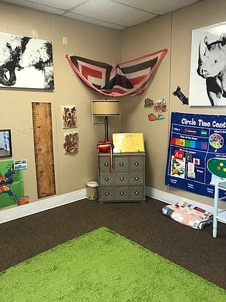Corner of a room with a green rug, wall art, and a small cabinet