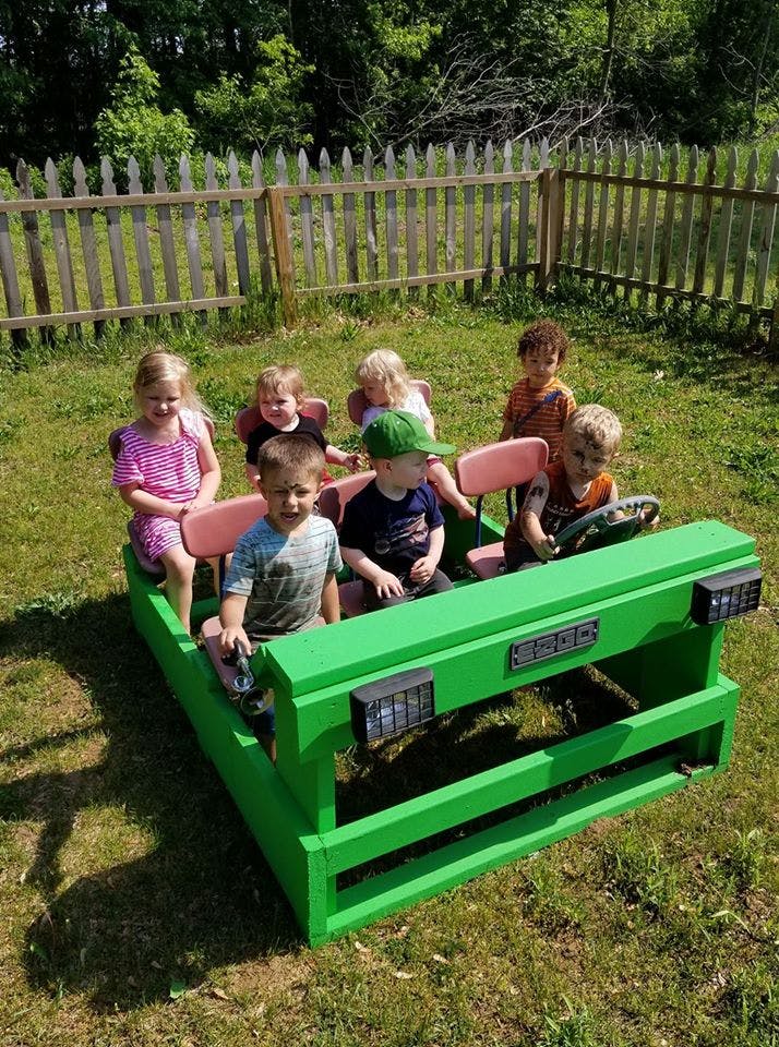 Children playing in a green wooden sandbox shaped vehicle in a grassy area