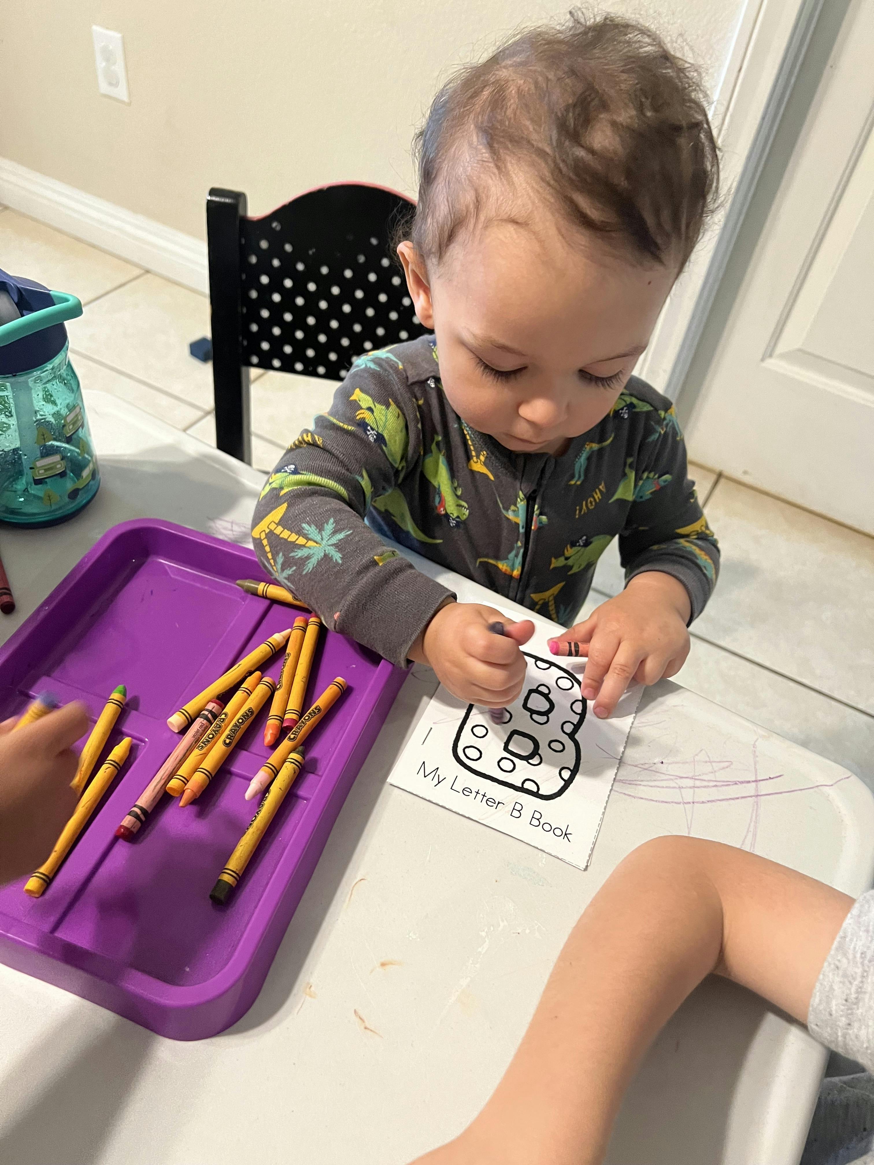 Child coloring a letter B on a paper with crayons