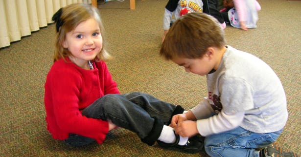 Child tying another child's shoe