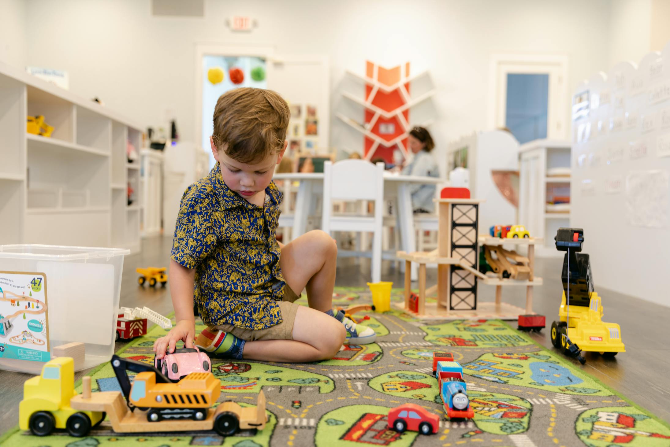 Child playing with toy trucks on a rug in a classroom