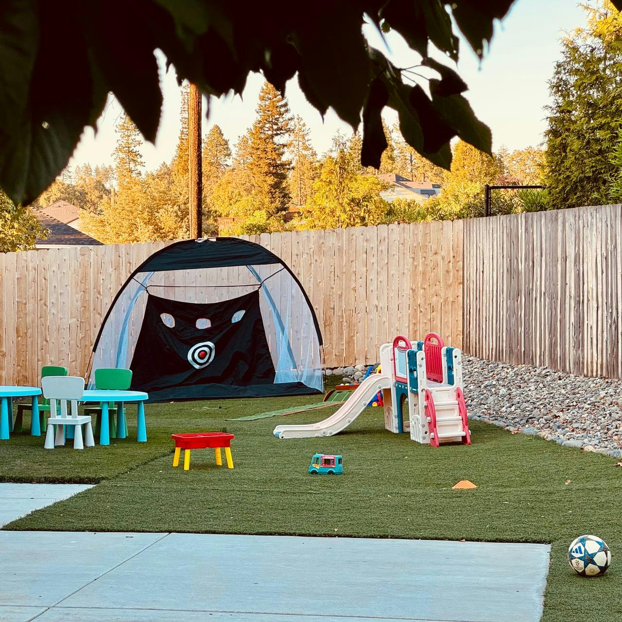 Backyard with a golf hitting net, playground slide, and children play furniture