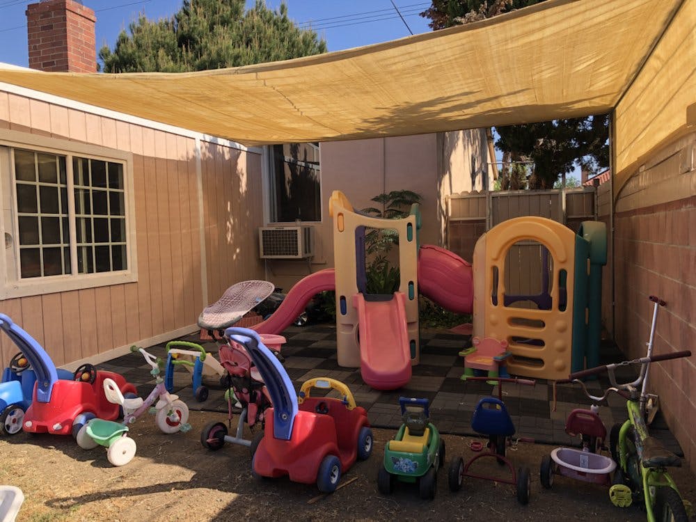 Outdoor play area with slides, play structures, and ride-on toys under a shade cover
