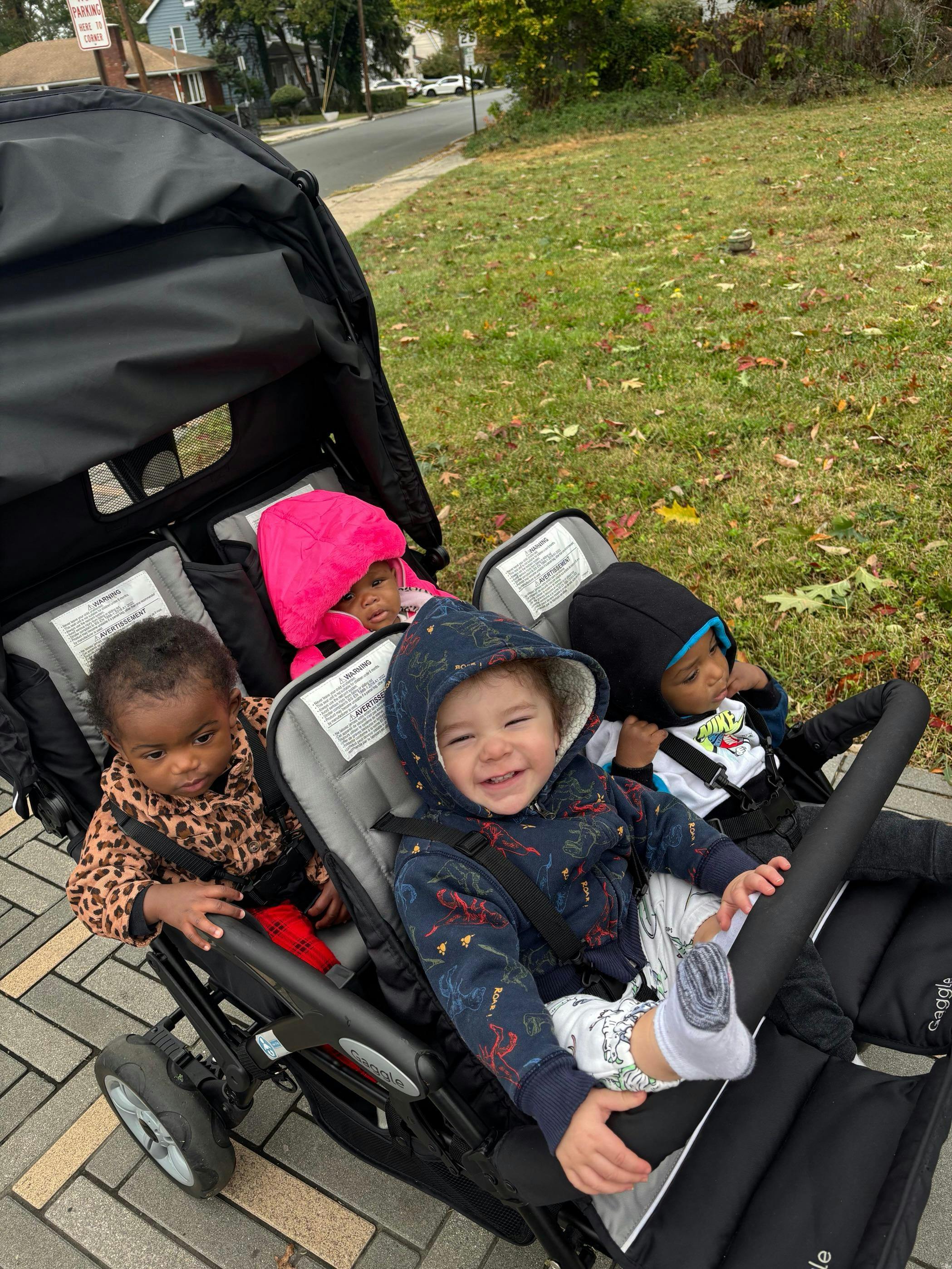 Four children in a quadruple stroller on a sidewalk