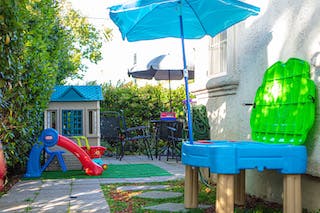 Play area with a blue umbrella, slide, playhouse, and water table