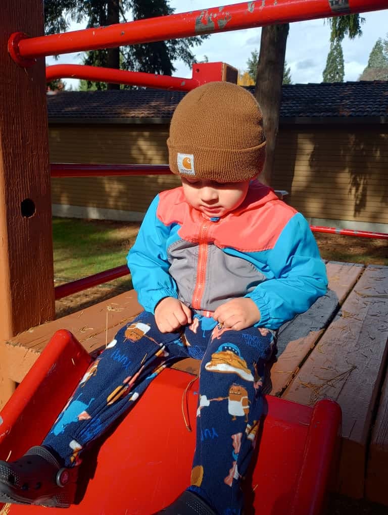 Child in a beanie sitting on a red slide