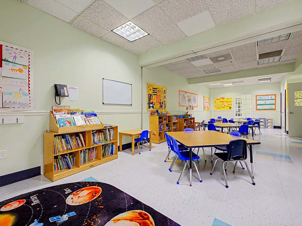 Classroom with small tables and chairs, a bookcase, and children's artwork on walls