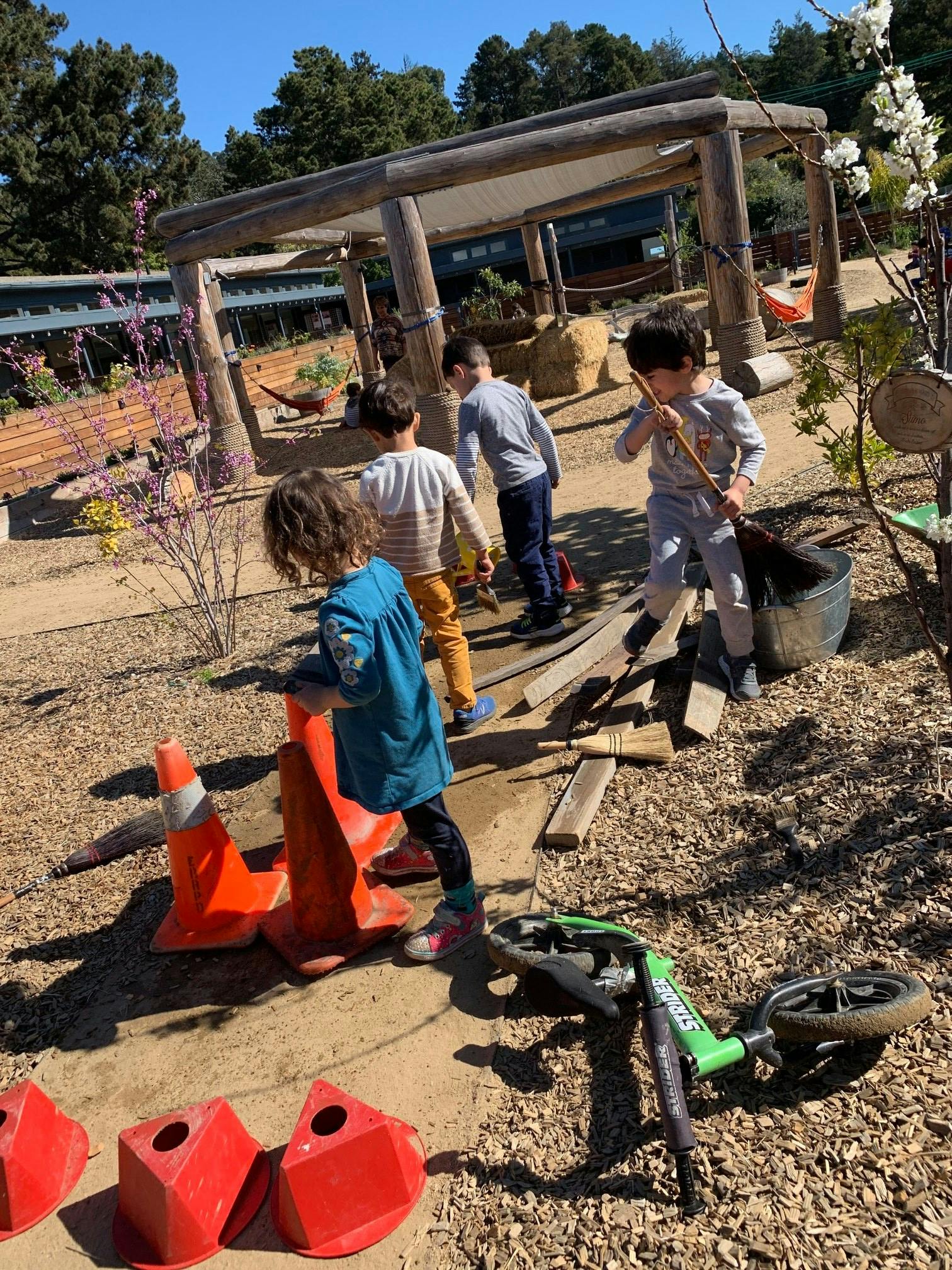 Children playing outdoors with brooms and orange cones