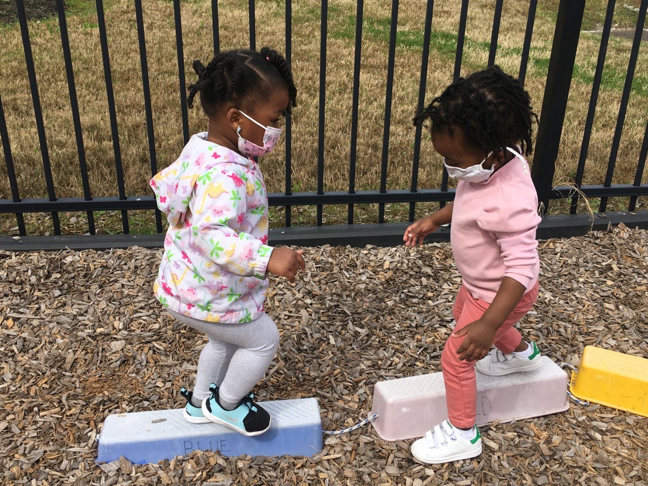 Two children in masks playing on stepping stones outdoors