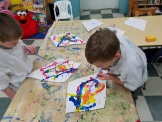 Two children painting at a table in a classroom