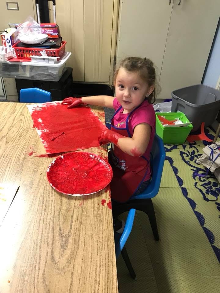 Child finger painting with red paint at a table
